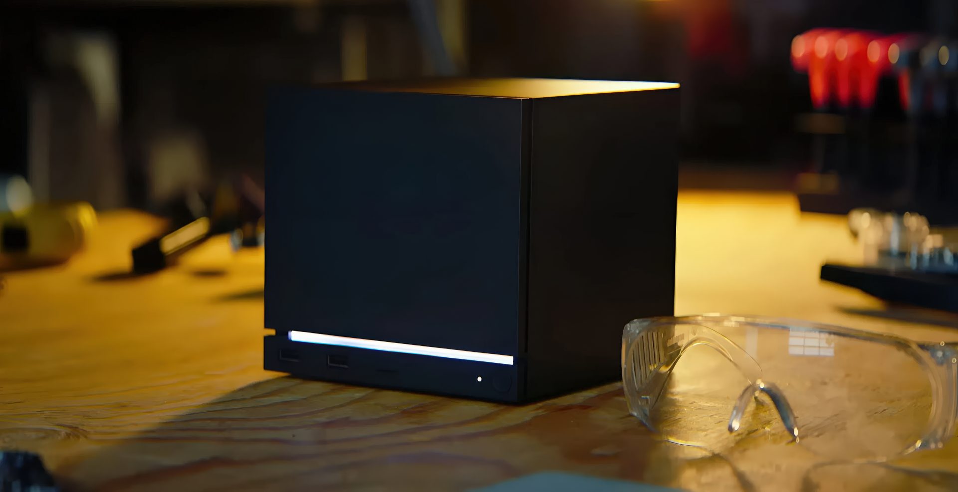A Steam Machine with a white LED light strip is placed on a wooden table next to a pair of safety glasses.