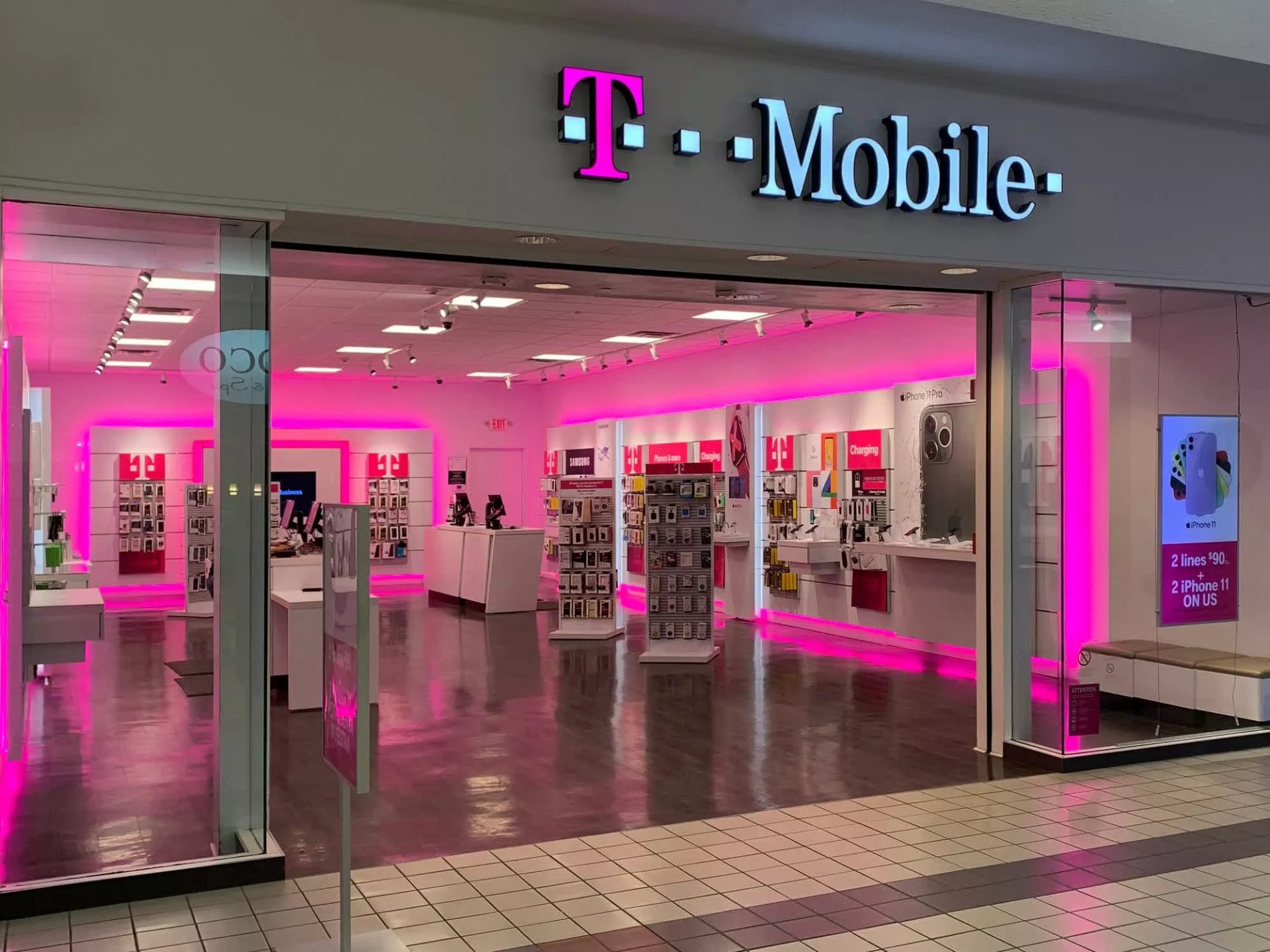 A T-Mobile retail store with a bright pink interior display advertising '2 lines $90' and 'iPhone 11 ON US.'