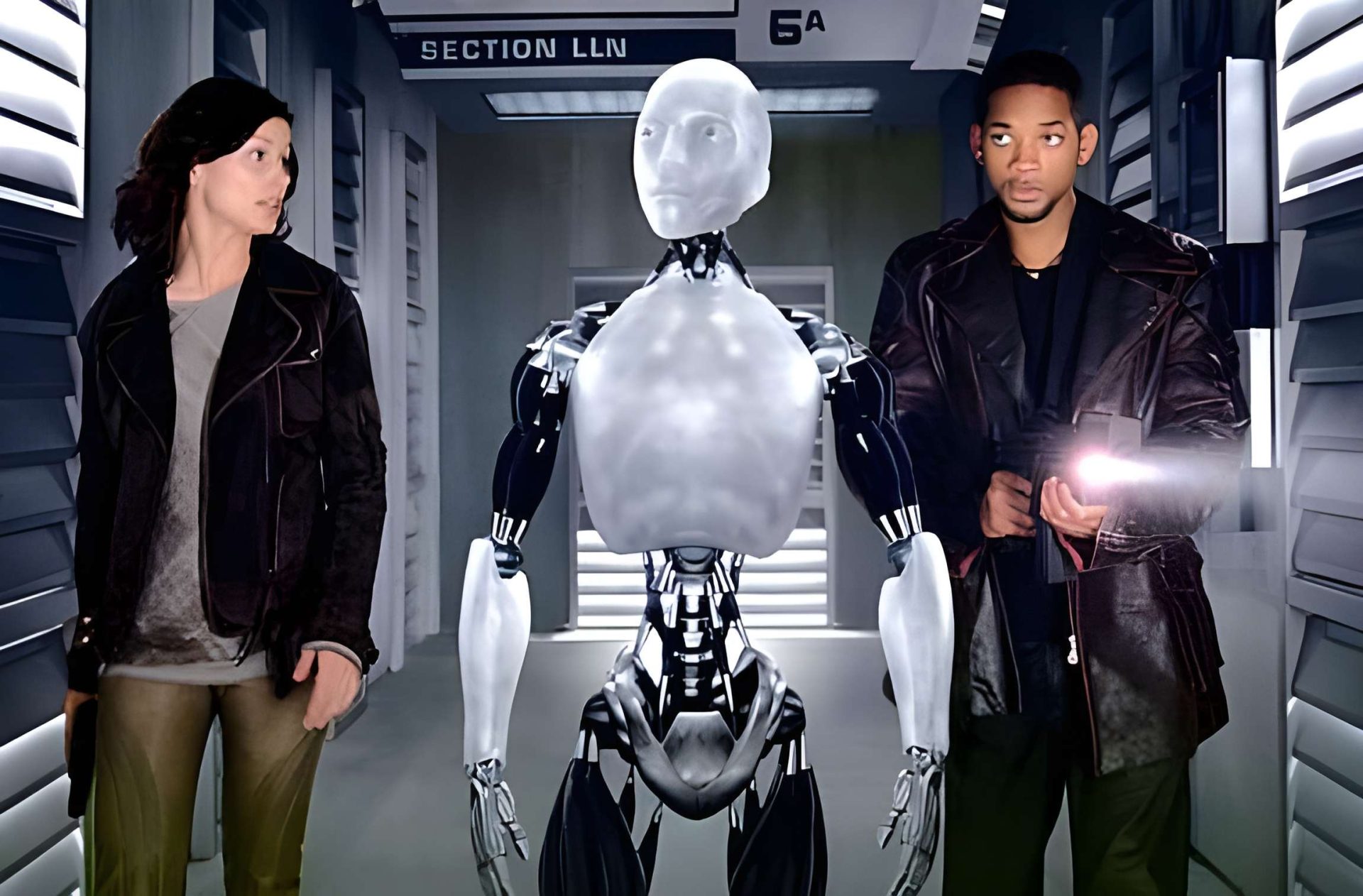 A humanoid robot stands between two people in a futuristic corridor labeled 'Section 6A'.
