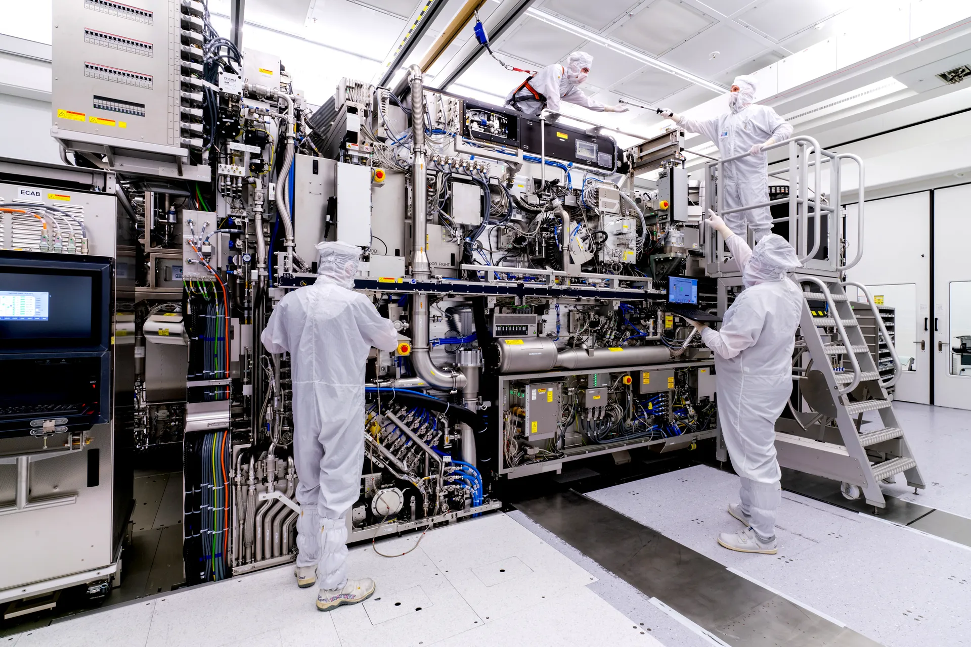 Technicians in cleanroom suits working on a large semiconductor manufacturing machine.