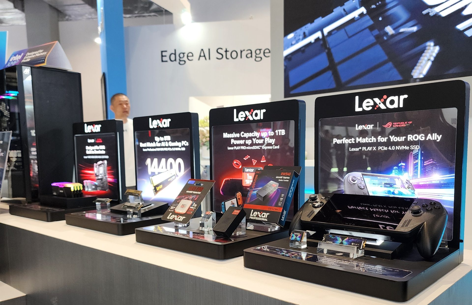 A display of Lexar products at a booth, featuring promotional signs for Lexar PLAY X PCIe 4.0 NVMe SSD and Lexar NSIO 600S microSD Express Card, with the text '14400' and 'Perfect Match for Your ROG Ally.'