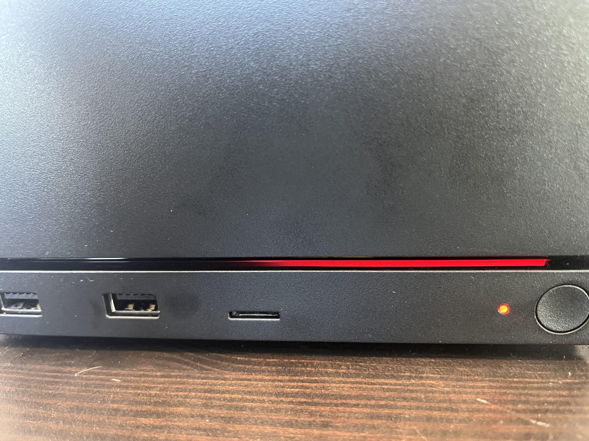The bottom section of a black PlayStation 4, showing USB ports, a power button, and a red light on a wooden surface.