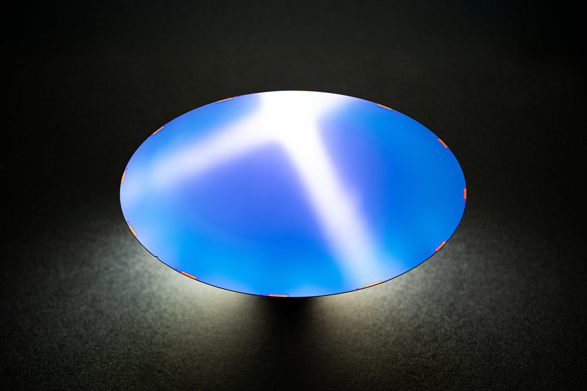 A polished semiconductor wafer with a blue reflective surface displayed against a dark background.