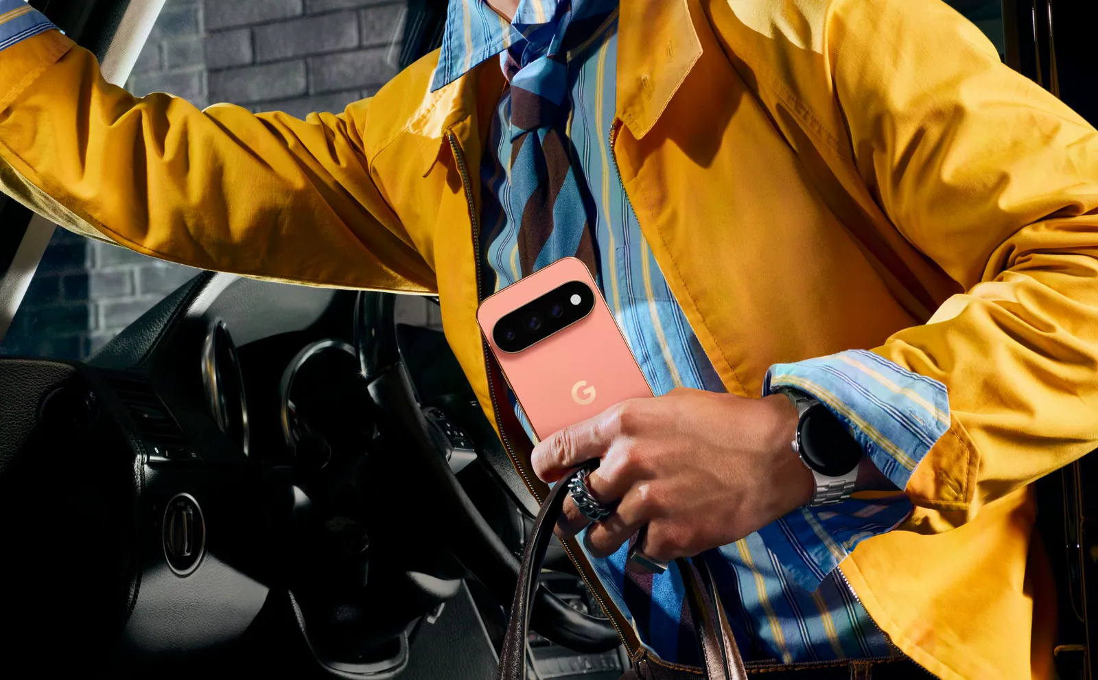 A person in a yellow jacket holding a pink Google Pixel 8 Pro phone inside a car.