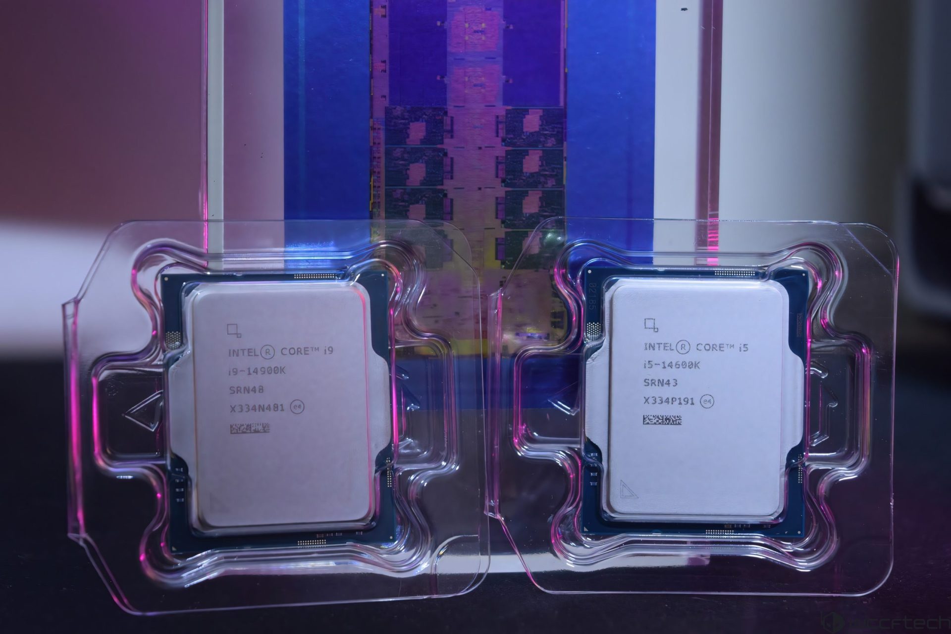 Two Intel processors, the Core i9-14900K and the Core i5-14600K, are displayed in their packaging against a blurred background of a processor wafer.