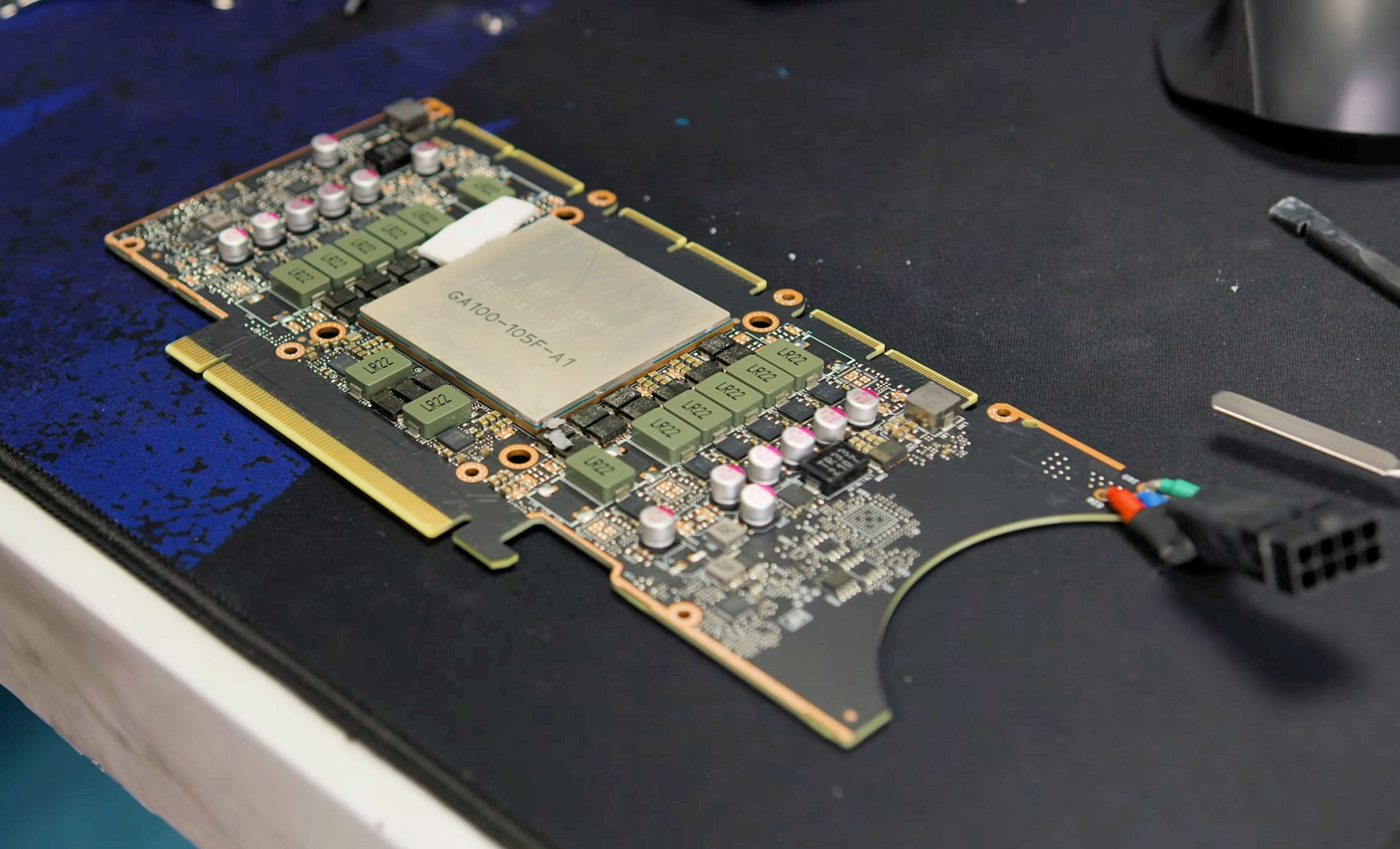 A close-up of a graphics card with an NVIDIA chip labeled 'GA100-105F-A1' on a cluttered workspace.