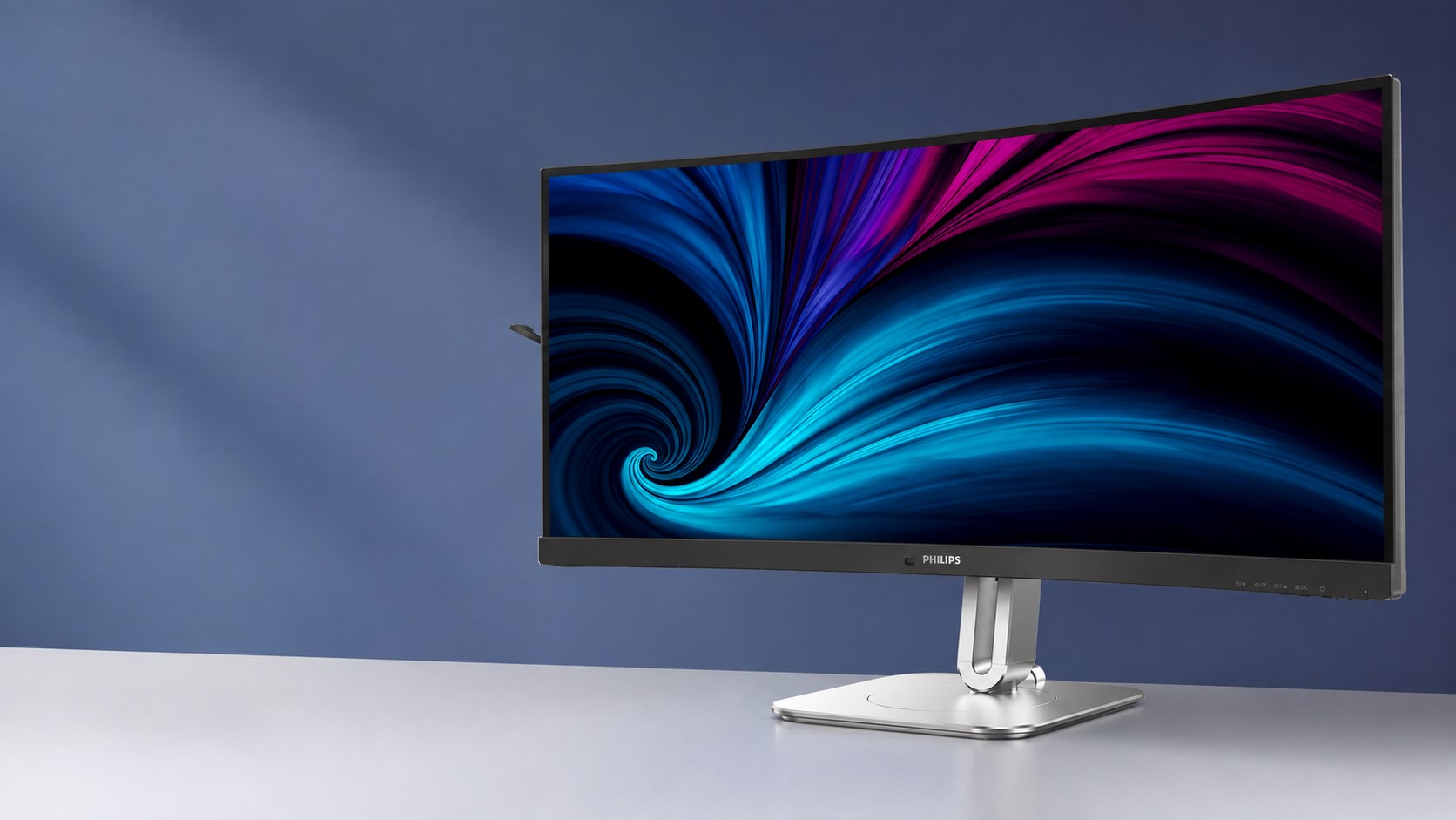 A Philips curved monitor with a vibrant blue and magenta swirl pattern on the screen sits on a sleek silver stand against a blue background.