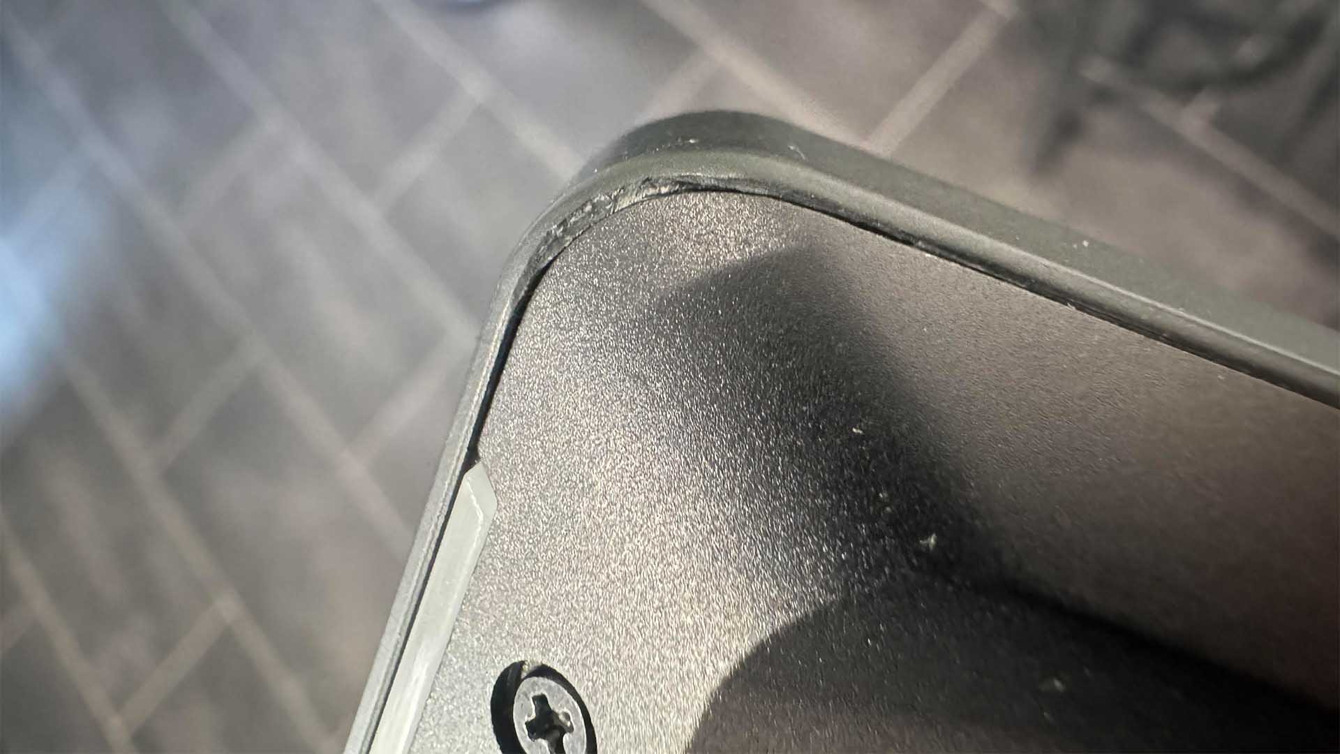 Close-up of a damaged corner on a black device showing chipped plastic and exposed inner material.
