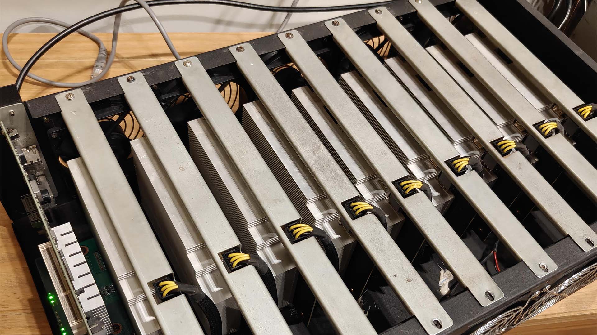 A mining rig with multiple unbranded GPUs secured in a metal frame, displaying yellow power cables and visible fan units.