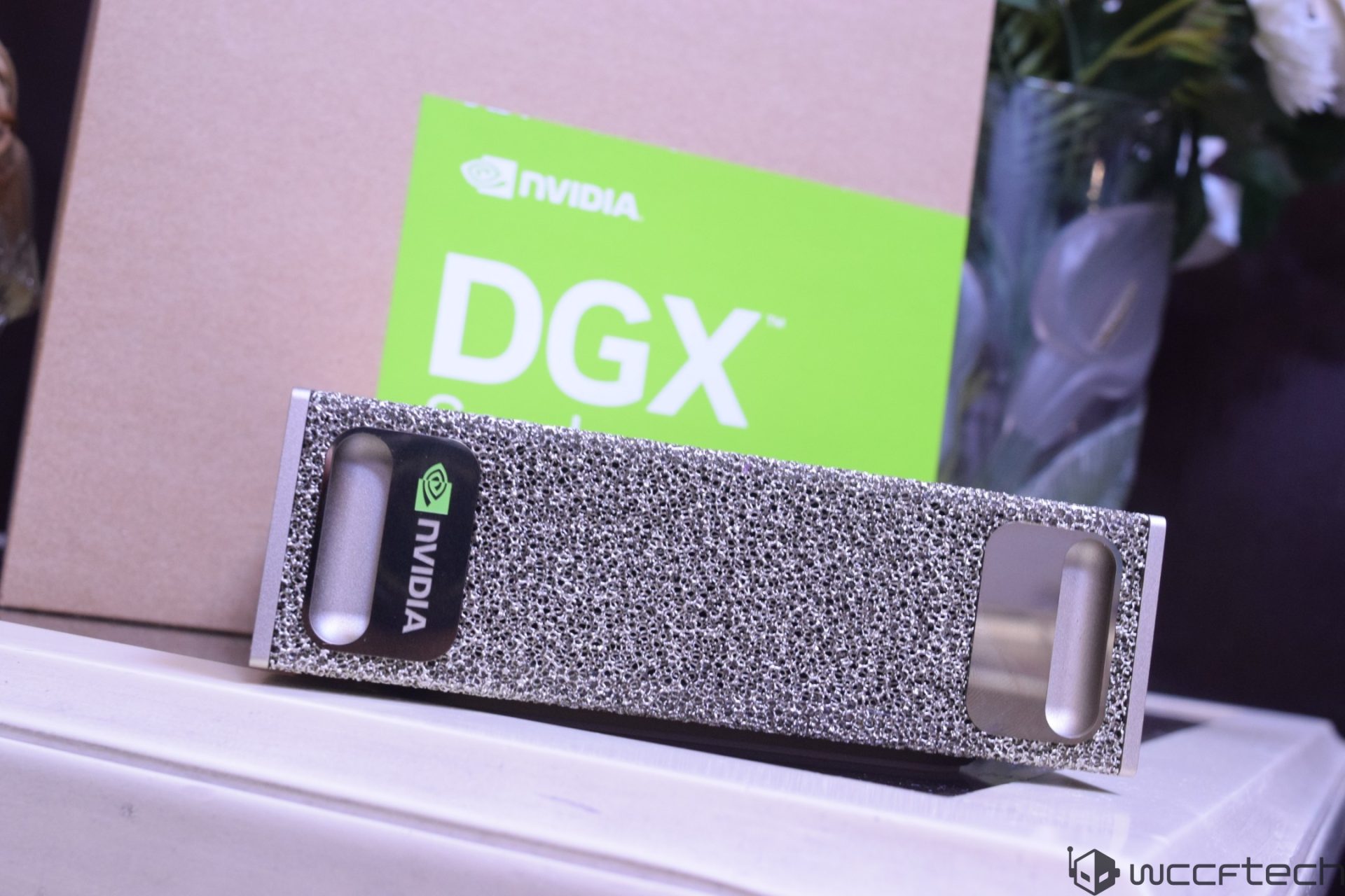 A textured metallic NVIDIA component is positioned in front of a 'NVIDIA DGX' branded box.