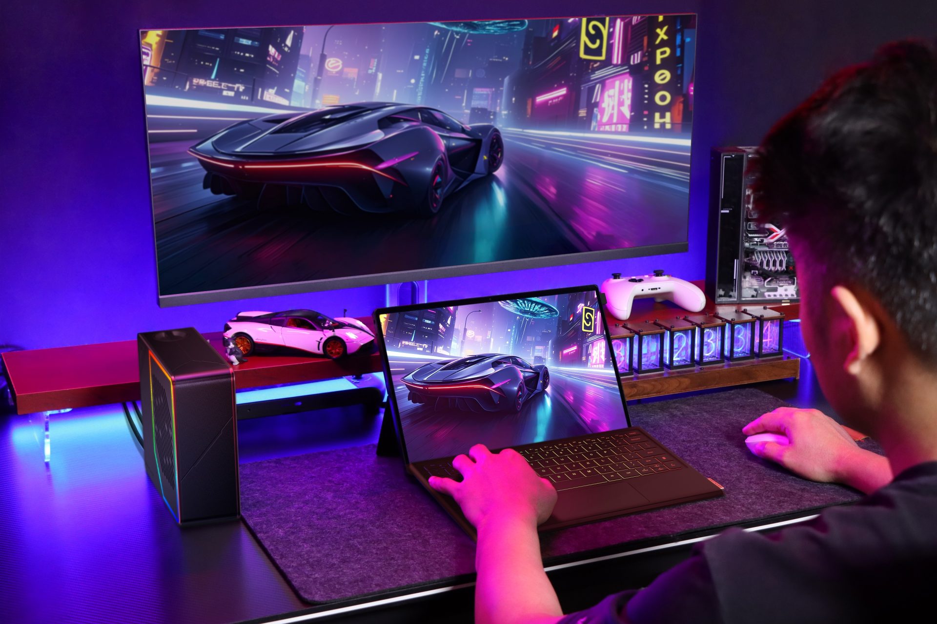 A person is using a laptop that displays a racing game with a sports car on a neon-lit city street, with the same image mirrored on a large monitor and a white gaming controller nearby.